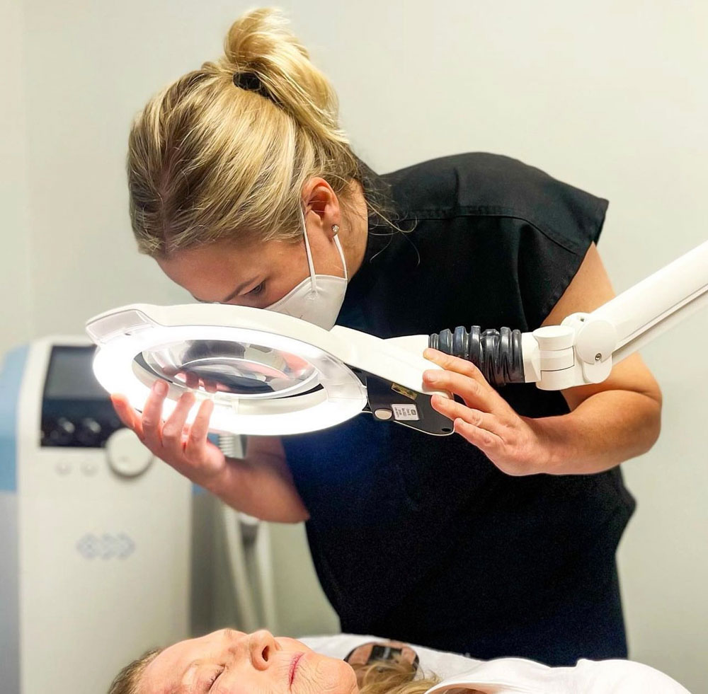An Advanced Skin Care clinician examining a client under a magnifying lamp